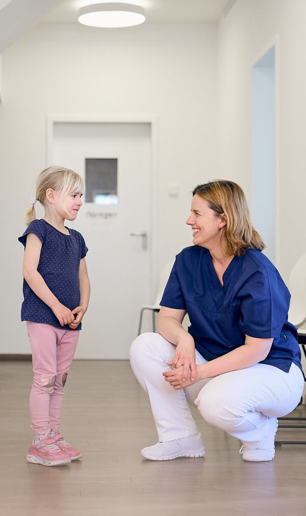 Zahn&auml;rztin Anna Rothe spricht auf Augenh&ouml;he mit einem kleinen M&auml;dchen im hellen Flur ihrer modernen Praxis in Breisach.