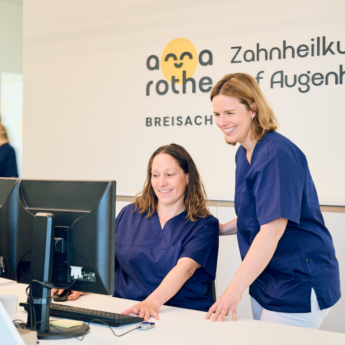 Frau Anna Rothe und eine Mitarbeiterin der Zahnarztpraxis Anna Rothe bei der gemeinsamen Arbeit am Computer im Empfangsbereich.