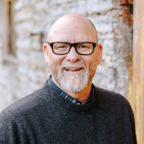Portrait eines 60-j&auml;hrigen Mannes in grauem Pullover, der freundlich in die Kamera l&auml;chelt.