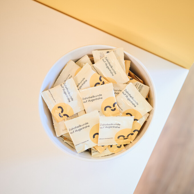 Wei&szlig;e Schale gef&uuml;llt mit Give-aways der Zahnarztpraxis Anna Rothe, beschriftet mit &bdquo;Zahnheilkunde auf Augenh&ouml;he&ldquo;.