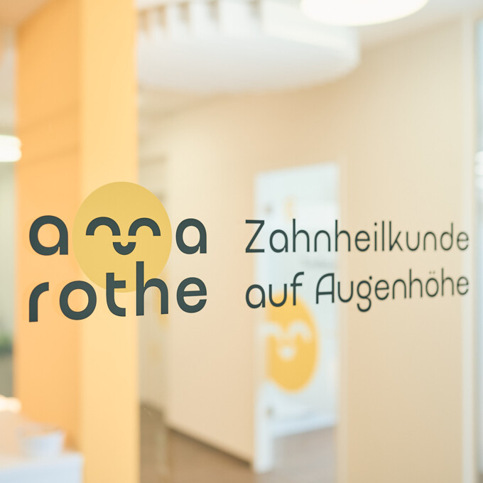 Logo der Zahnarztpraxis Anna Rothe mit dem Slogan &bdquo;Zahnheilkunde auf Augenh&ouml;he&ldquo; als Glasfolierung in der modern gestalteten Praxis.